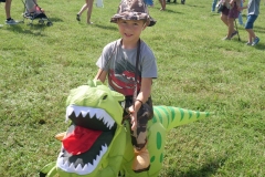 Child wearing an inflatable dinosaur costume smiles while participating in Cape Coral Kiwanis KidsFest 2025.