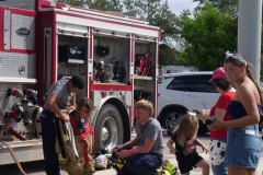 Firefighters help children explore firefighting gear beside a fire truck at Cape Coral Kiwanis KidsFest 2025.