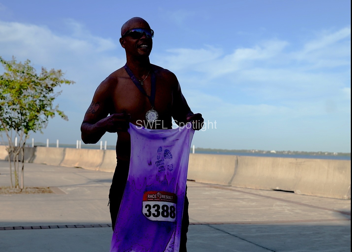 Purple Color Run finisher proudly displays medal and race shirt after completing the event in Fort Myers.