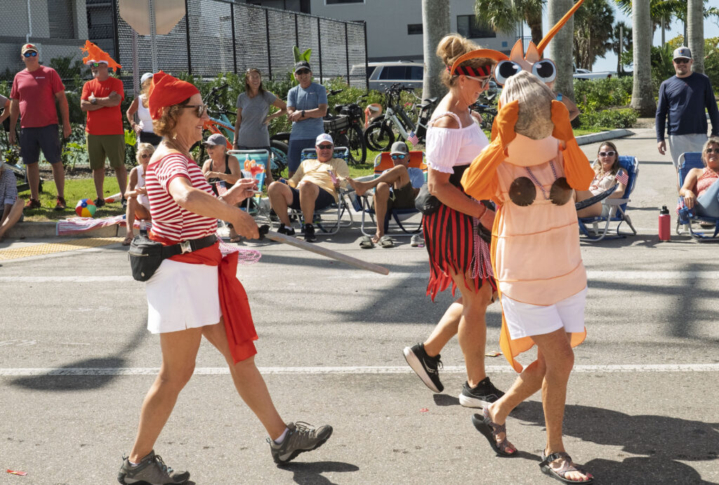 Costumed parade participants dressed as shrimp and pirates entertain spectators during the 68th Annual Fort Myers Beach Lions Club Shrimp Festival Parade. The image captures the fun, family-friendly atmosphere that has become a hallmark of the festival while celebrating the island's commercial shrimping heritage through creative and humorous parade entries.