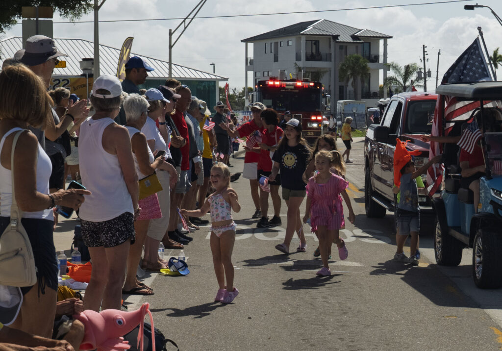 Children smile and wave American flags as they interact with parade participants during the 68th Annual Fort Myers Beach Lions Club Shrimp Festival Parade on Estero Boulevard in Fort Myers Beach, Florida.