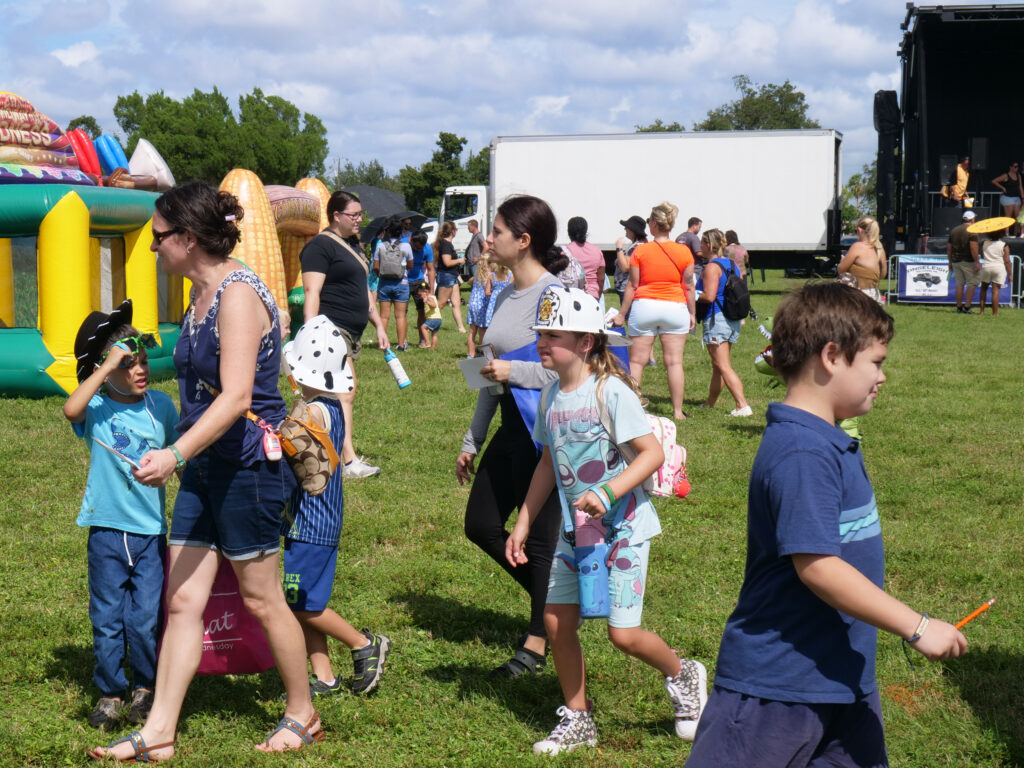 Families and children walk across a grassy field near inflatable play structures at KidsFest in Cape Coral.
