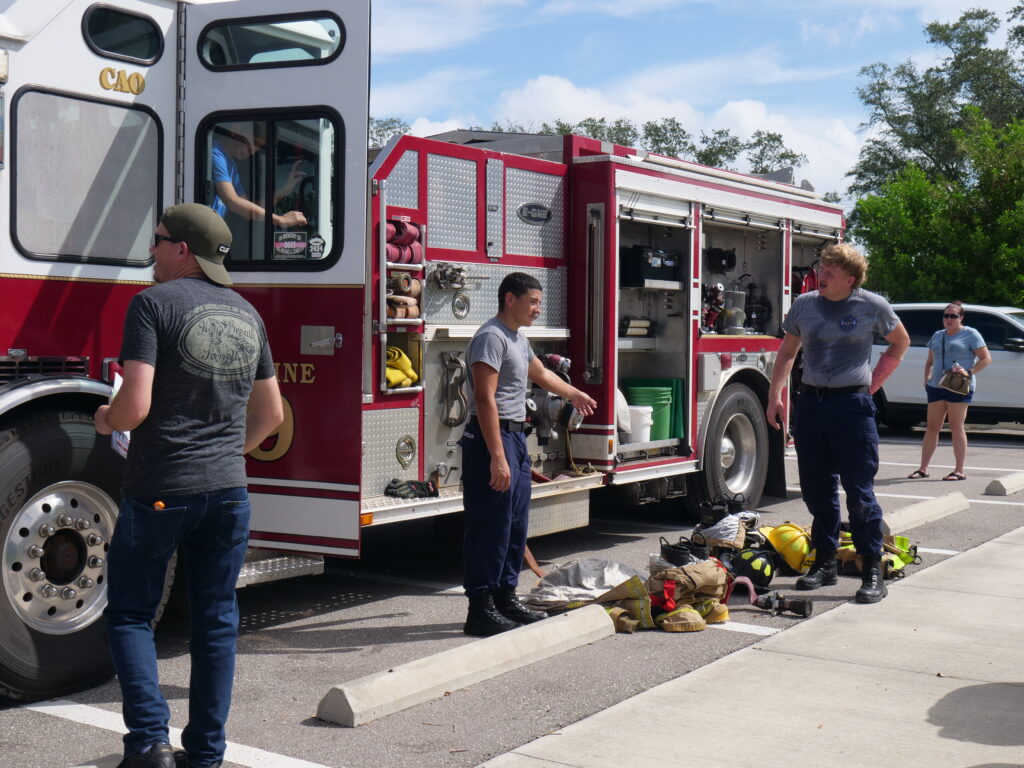 Firefighters demonstrate gear and equipment beside a fire truck at a community event in Cape Coral.