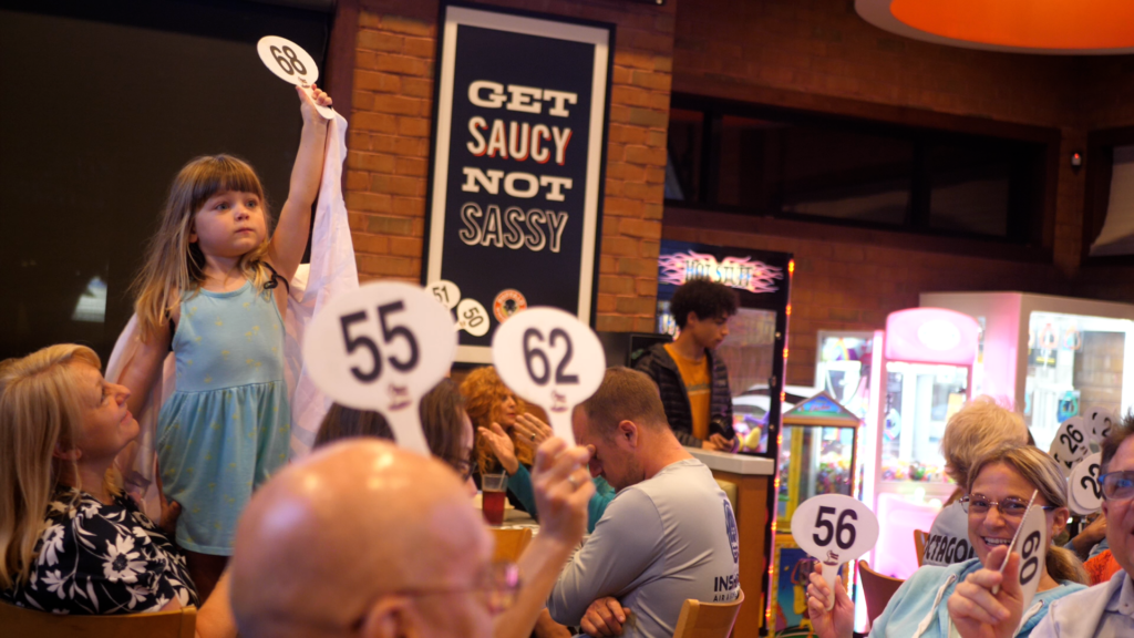 A young attendee raises a bidding paddle during the Rebel Riders Charities quarter auction at Wings and Rings in Fort Myers, Florida.